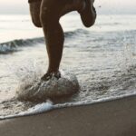 Dynamic shot of legs running on Palanga beach during sunrise, splashing water.